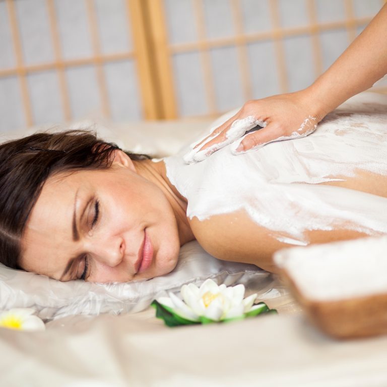 Massage therapist applying rehydrating body wrap over woman's back.