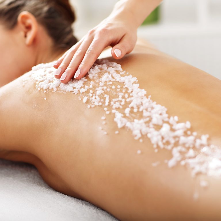 Woman having sea salt layered and scrubbed over her back by a therapist.